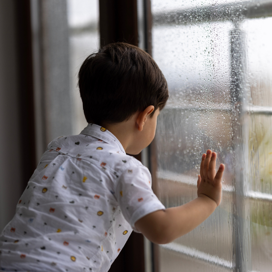 Young child looking through a rain-covered window on a gloomy day.