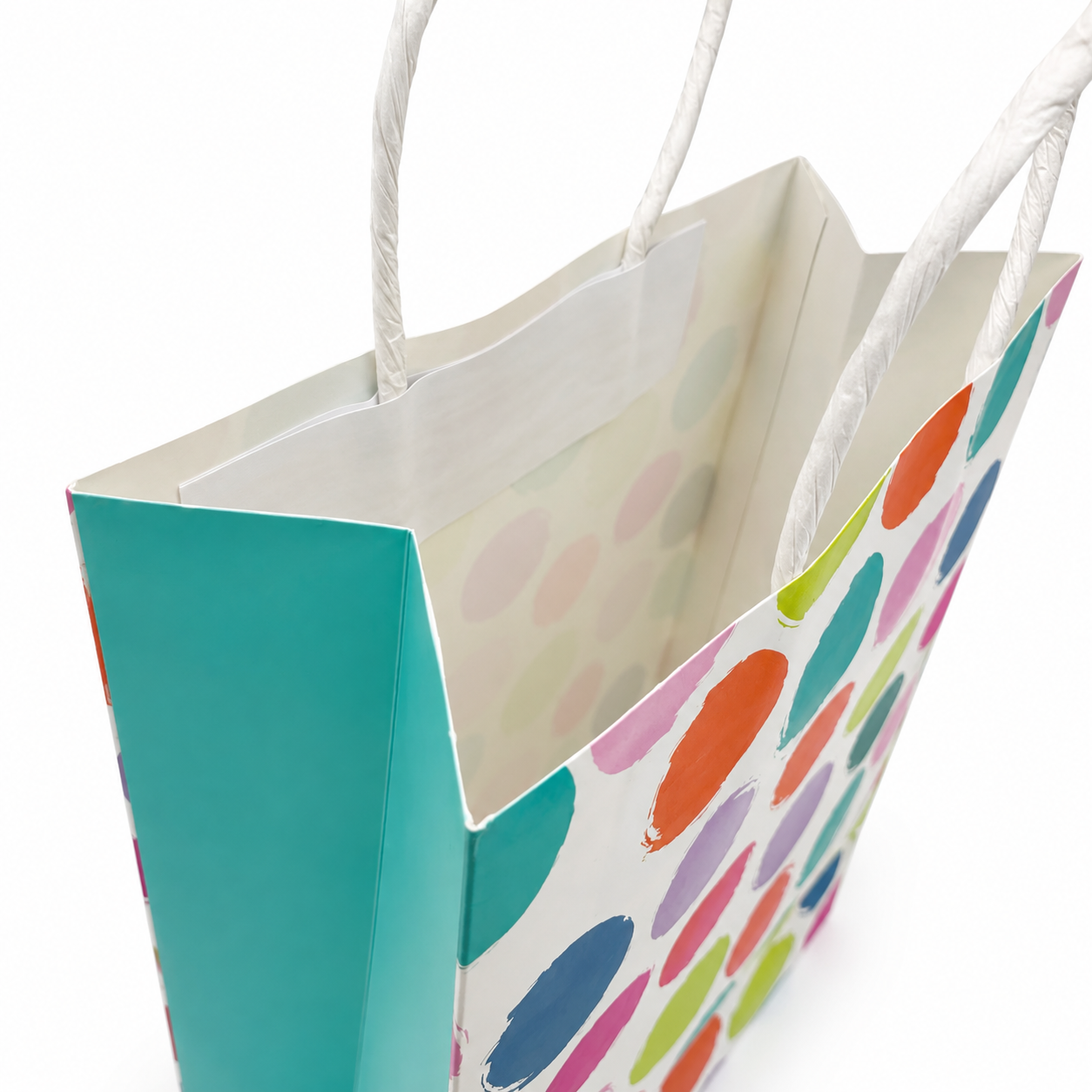 A paper gift bag with white twisted rope handles, featuring a white exterior decorated with colorful painted polka dots and a solid turquoise side panel, shown on a white background.
