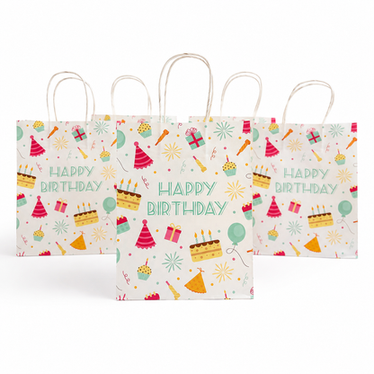 Three white paper gift bags with natural kraft handles, decorated with colorful 'HAPPY BIRTHDAY' party illustrations including cakes, balloons, hats, and fireworks, arranged on a white background.
