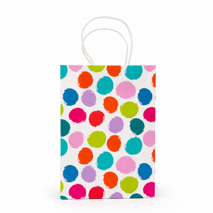 A small paper gift bag with white twisted handles, featuring a colorful pattern of hand-painted style polka dots in pink, blue, orange, green, and purple on a white background.