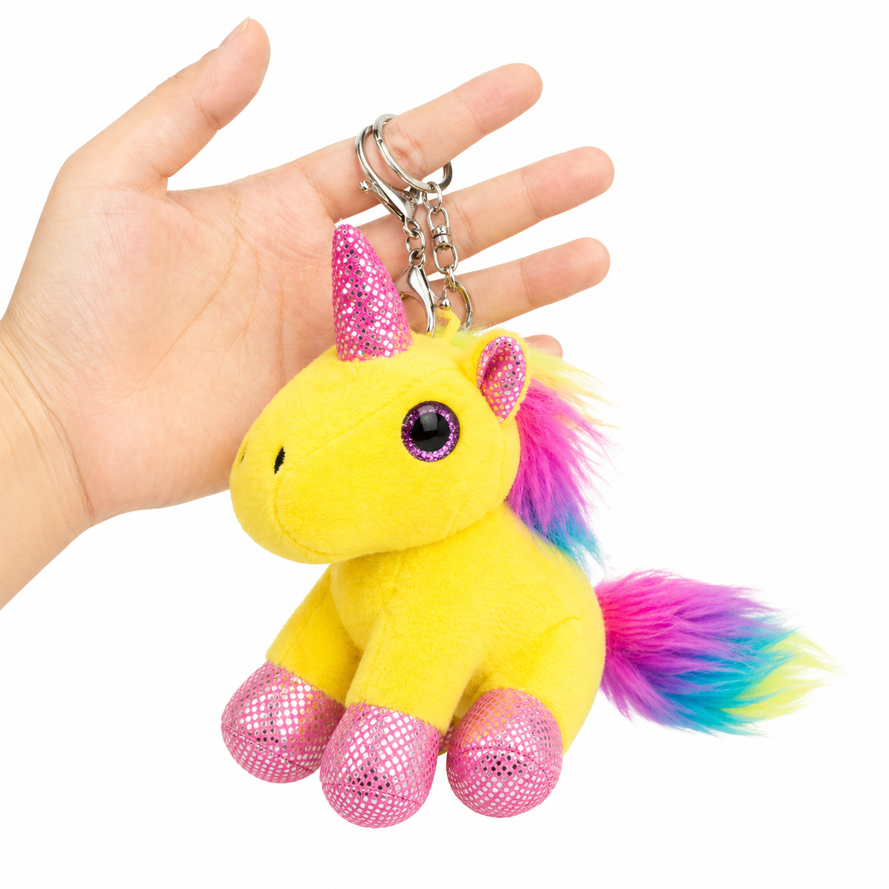 Yellow plush unicorn keychain with pink glittery accents held in a hand against a white background